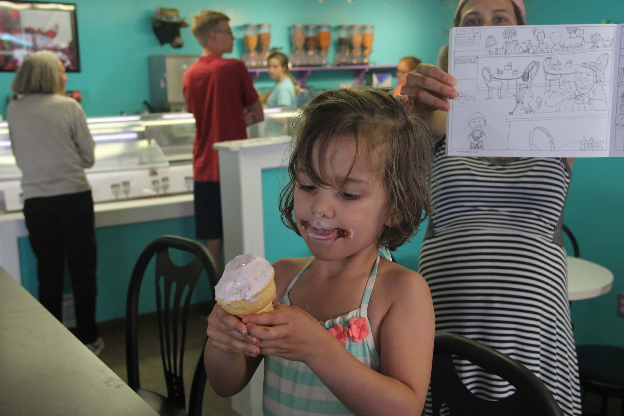 Our middle kiddo enjoys her ice cream cone inside the Island Creamery, while Joanna holds up the "Inside the Creamery" page of her book.